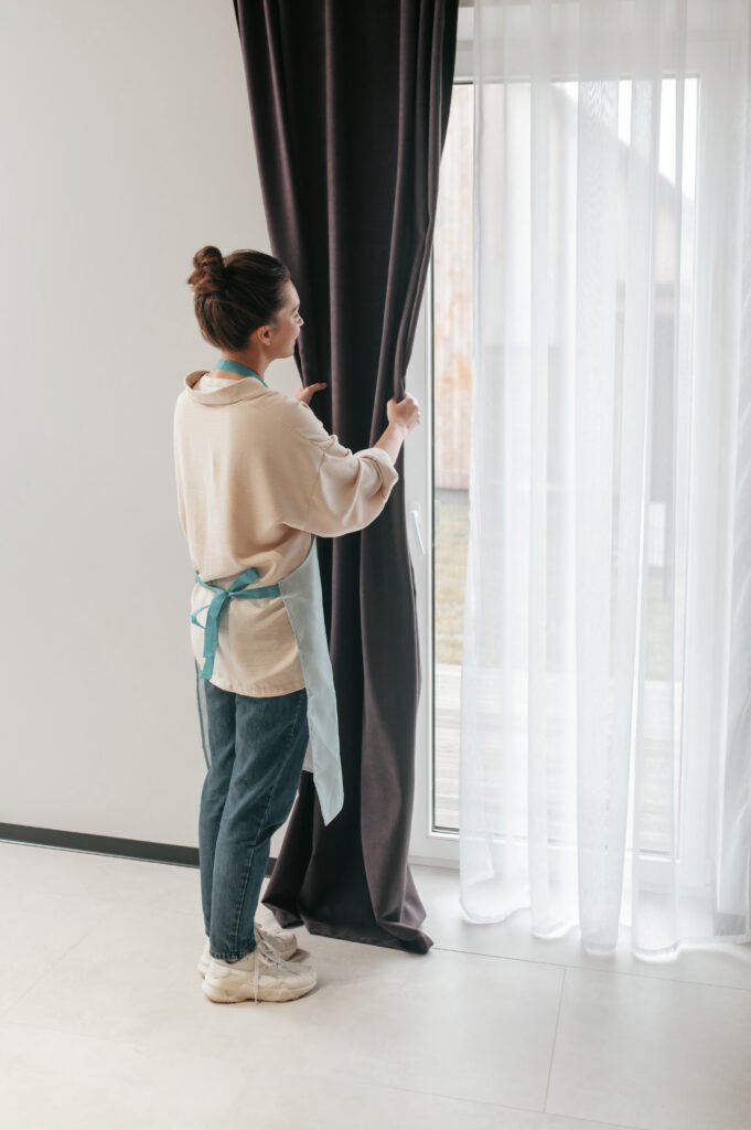 Young Woman Standing Near Widnow Fixing Curtains 681x1024